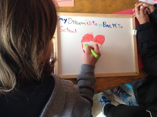 Refugee child writing 'My dream is to go back to school' on a board.
